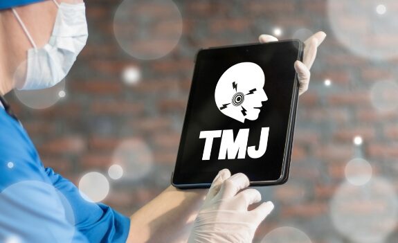 Dentist holding tablet with model of the jaw and the letters T M J on screen