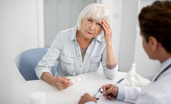 Senior woman touching her temple in pain while talking to doctor