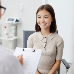 Woman smiling while doctor writes on clipboard