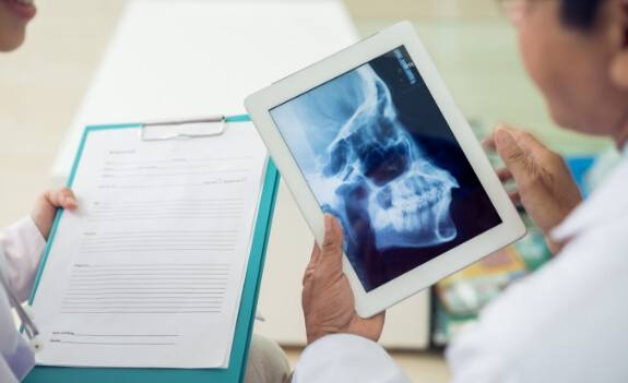 Doctor holding clipboard with forms next to doctor holding tablet with x ray of jaw