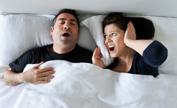 Woman covering her ears next to snoring man