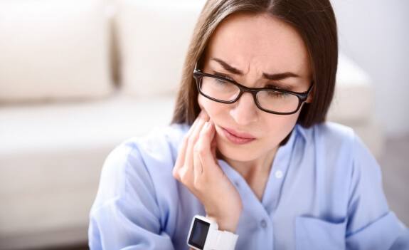 WOman in blue shirt holding side of her jaw in pain