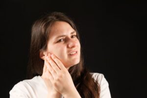 Woman with TMD pain, pictured against dark background