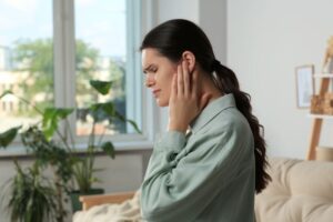 Woman sitting on sofa, experiencing ear pain 